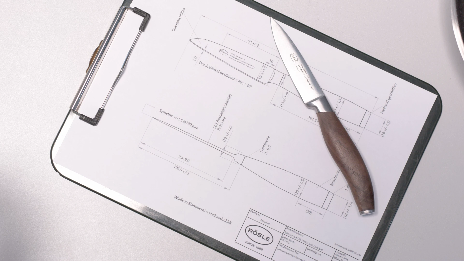 Entwurf eines Küchenmessers auf einem Klemmbrett mit technischer Zeichnung und Messer, erstellt von Bürobewegt.