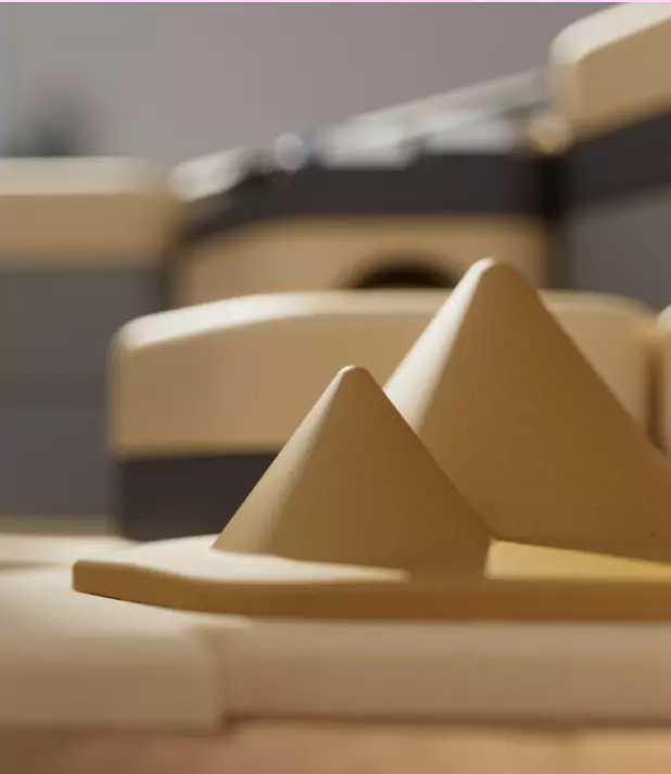 Zwei gelbe, konische Spielzeugpyramiden im Vordergrund, unscharfer Hintergrund mit Möbeln in warmen Tönen.