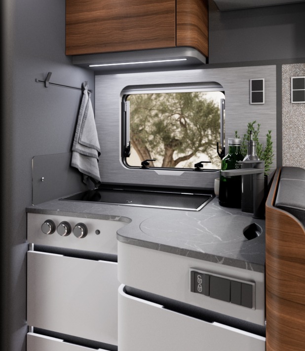 Wohnmobilküche mit moderner Arbeitsplatte, Gasherd, Spüle und Fenster mit Blick ins Grüne.