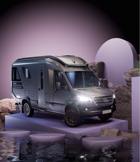 Silbernes Wohnmobil auf modern inszenierter Kulisse mit reflektierendem Wasser und geometrischen Elementen im Hintergrund.