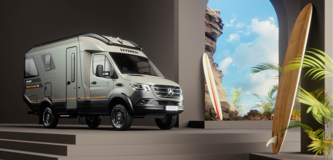 Wohnmobil Hymer Venture S im modernen Raum mit Surfbrettern und Ausblick auf Felsenlandschaft und blauen Himmel.