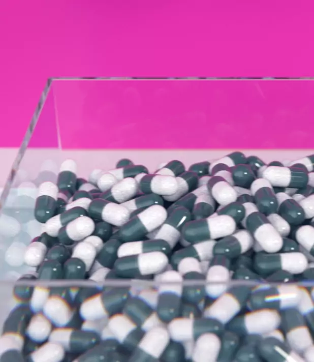 Grüne und weiße Kapseln in einem Glasbehälter vor einem pinkfarbenen Hintergrund.