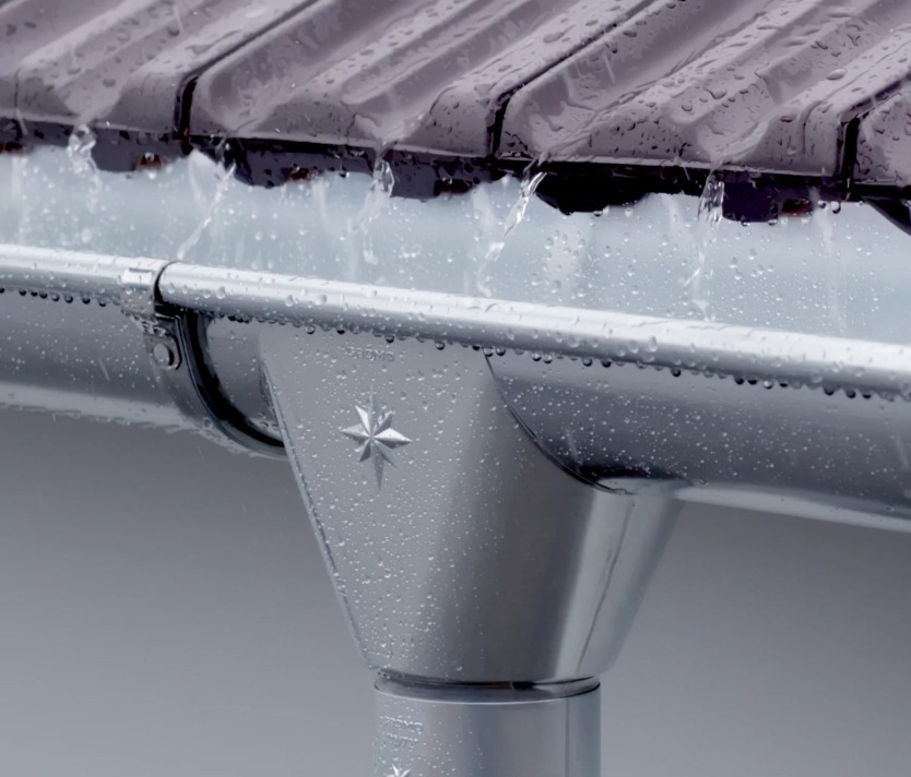 Metallregenrinne mit Regentropfen und Wasserfluss an einem Dach, Nahaufnahme für hochwertige Wasserableitungssysteme.