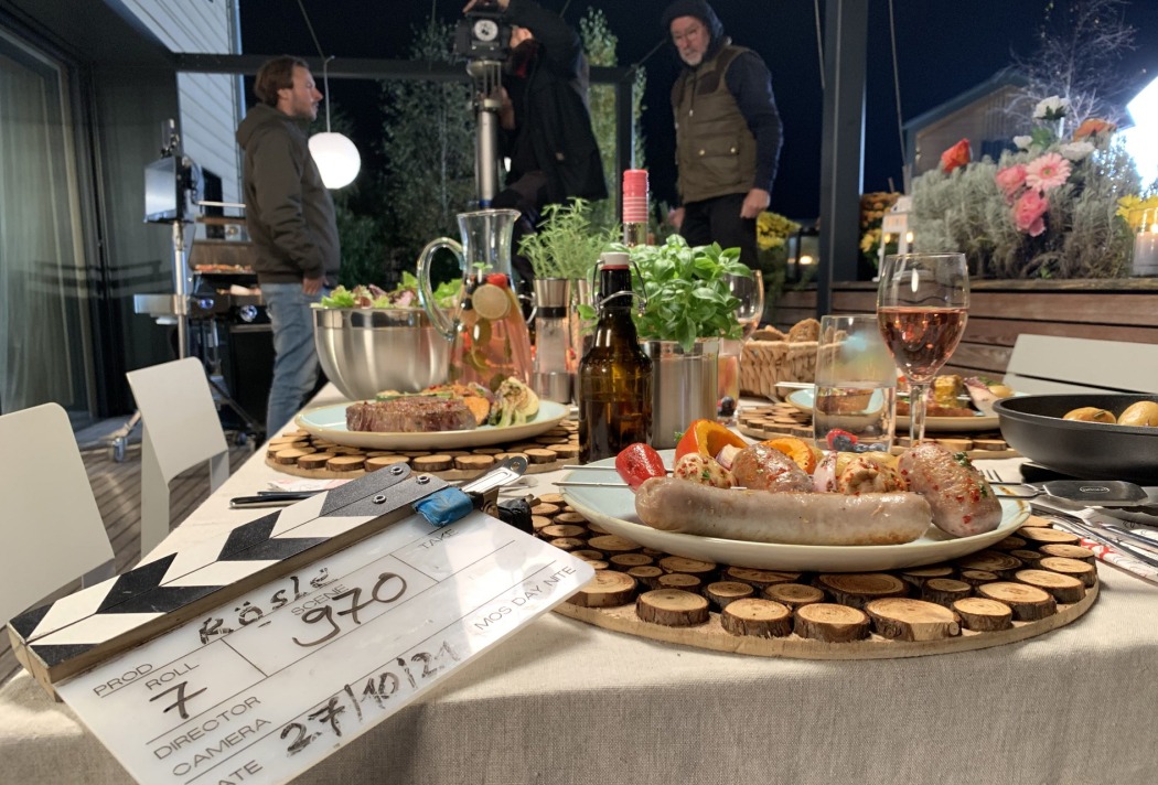 Filmset mit gedecktem Tisch, Speisen und Getränken bei Nacht im Freien, Personen im Hintergrund beim Filmen.