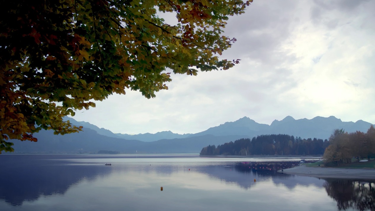 Bergsee Landschaft im Herbst mit buntem Laub, spiegelndem Wasser und Bergpanorama im Hintergrund.