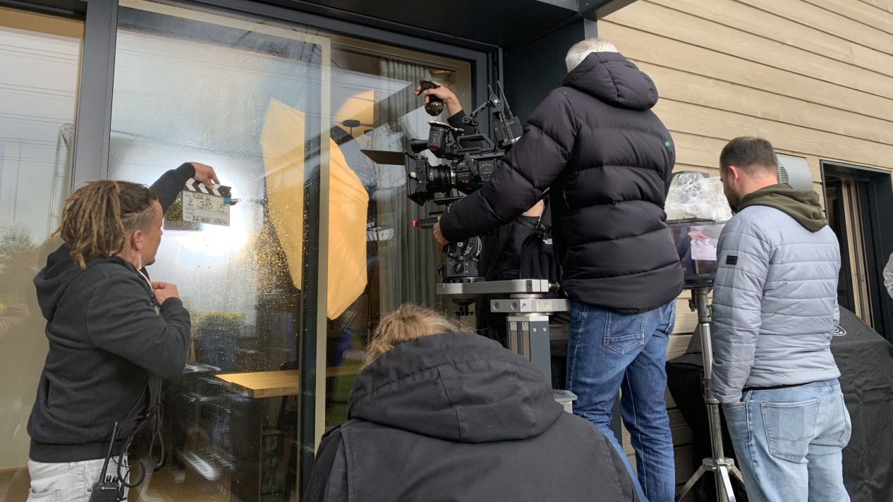 Filmcrew beim Drehen einer Szene mit Kameraausrüstung und Klappe vor einem Fenster.