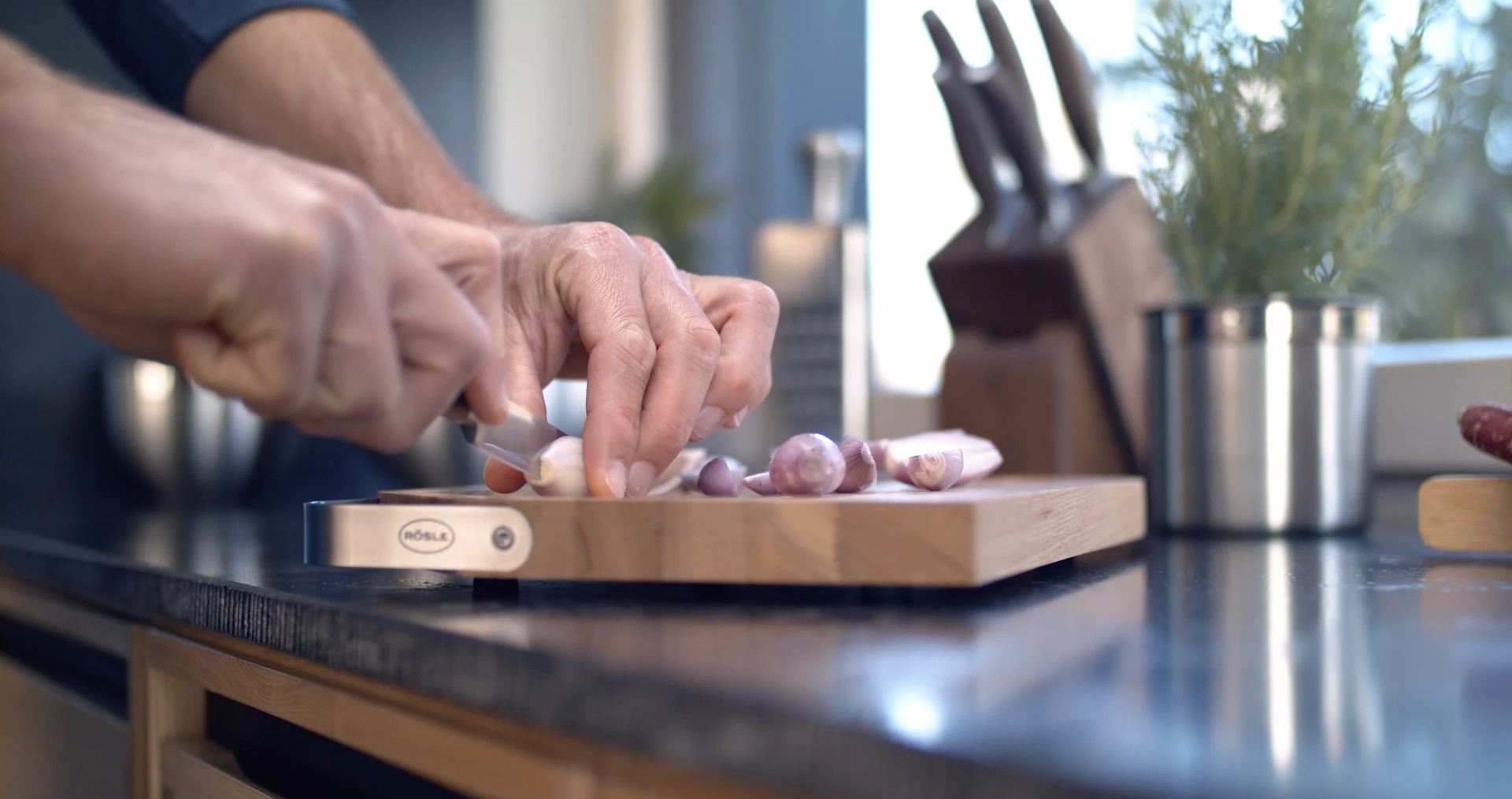 Benutzer schneidet Schalotten auf einem Holzbrett in moderner Küche.