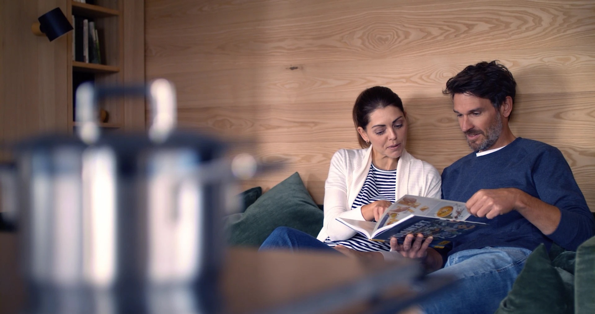 Paar sitzt auf Sofa und liest ein Kochbuch, entspannte Atmosphäre in modernem Wohnzimmer.