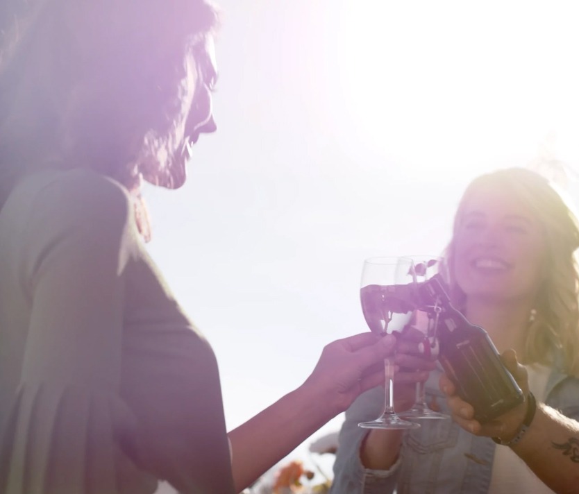 Freundinnen stoßen bei Sonnenschein mit Wein und Bier an, fröhliche Sommerstimmung im Freien.