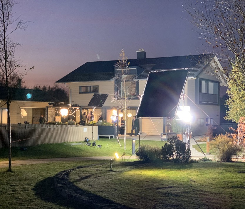 Filmset im Garten eines Hauses bei Nacht, mit Beleuchtung und Drehteam im Einsatz.