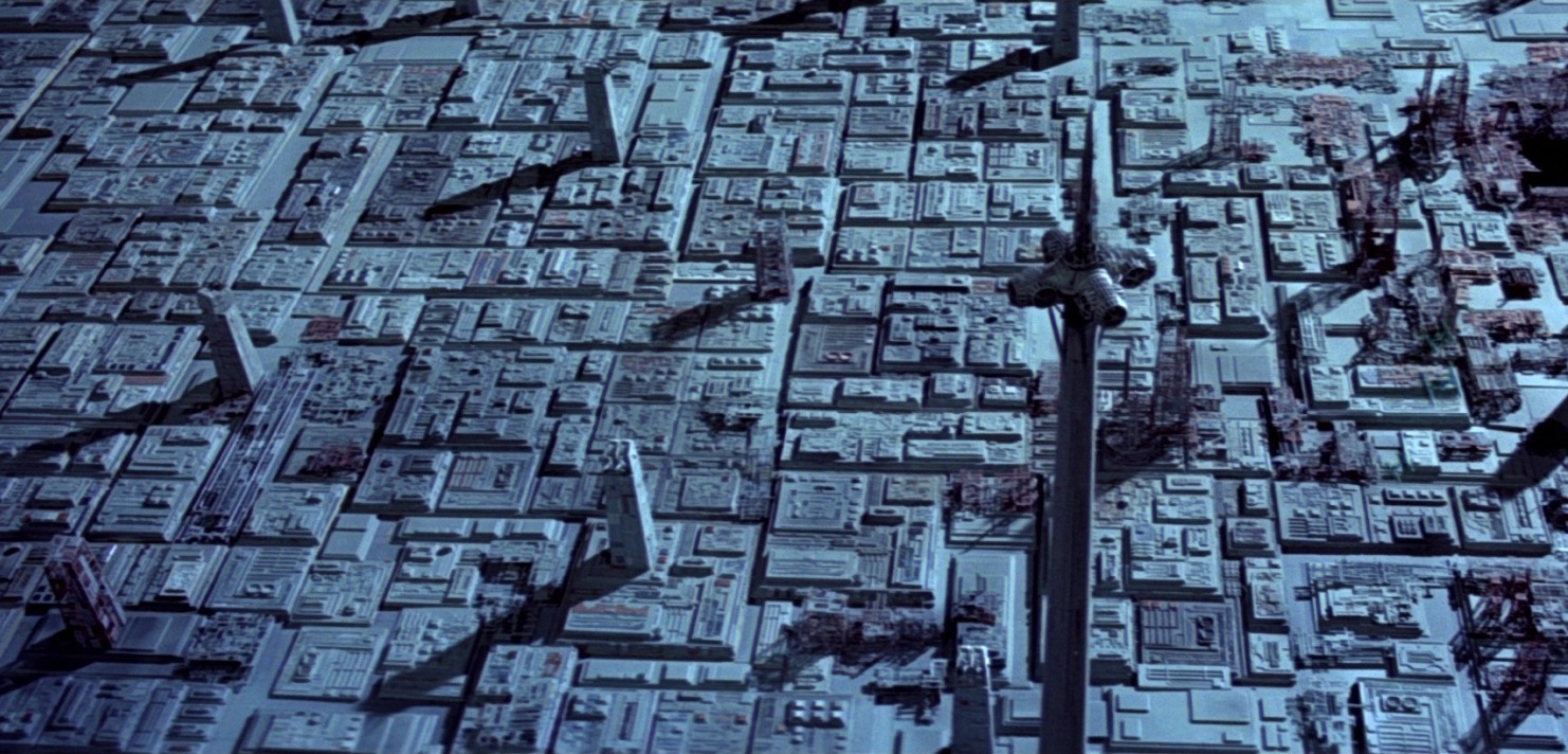 Futuristische Stadtlandschaft aus der Vogelperspektive mit vielen quadratischen Gebäuden und langen Schatten.