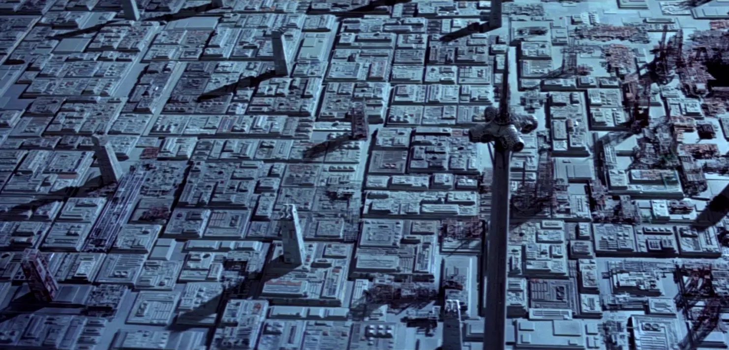 Futuristische Stadtlandschaft aus der Vogelperspektive mit vielen quadratischen Gebäuden und langen Schatten.