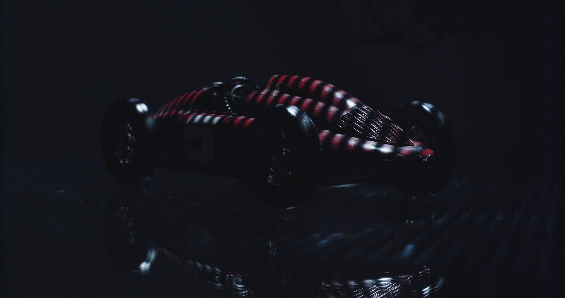 Schwarzes Retro-Spielzeugauto mit roten Streifen, Reflektion auf dunkler Oberfläche, modernes Design.